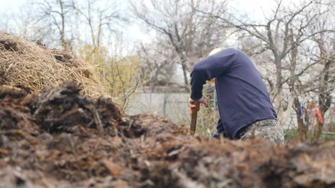 A man in a yellow cap throws the dung with a pitchfork. Countryside. Slow motion Stock Footage 126993116
