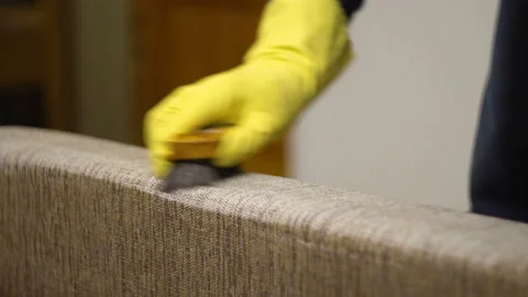 A man in a yellow glove cleans the back of the sofa 4K Video stock 142333385