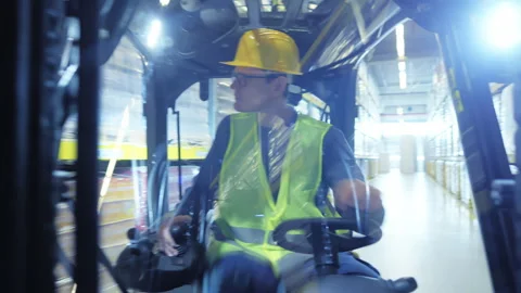 Man in yellow hard hat and vest drives a forklift in a warehouse. Vidéo 307998070