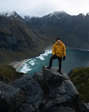 Man in yellow jacket on cliff ledge at Kvalvika Beach at sunset in Lofoten Stock Photos