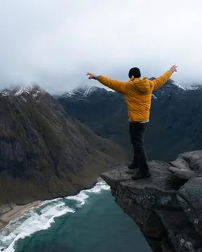 Man in yellow jacket on cliff ledge at Kvalvika Beach at sunset in Lofoten Stock Photos