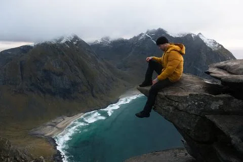 Man in yellow jacket on cliff ledge at Kvalvika Beach at sunset in Lofoten Stock Photos