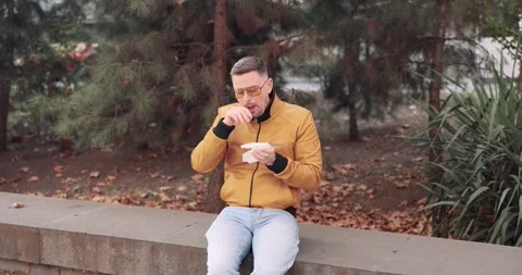 Man in yellow jacket sits on parapet using tissue to wipe nose Vidéo 312161577