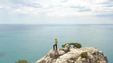 A man in yellow jacket stands on top of the rock against the beautiful sea co Stock Footage 165338916