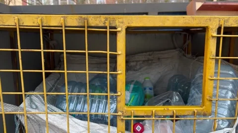Man in yellow jacket throws plastic lemonade bottle into metal container Stock Footage 271078532