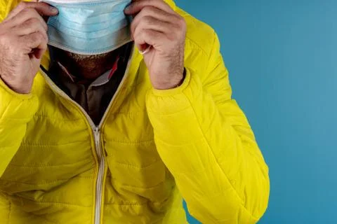 Man in yellow jacket is using a protective mask against corona virus on blue  Stock Photos