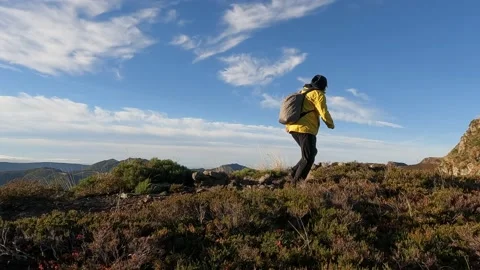 The man in the yellow jacket is walking along the mountain path at sunrise, i Video stock 219888807