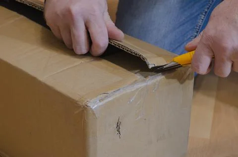 Man with yellow knife opens parcel in closed rectangular cardboard box on the Stock Photos