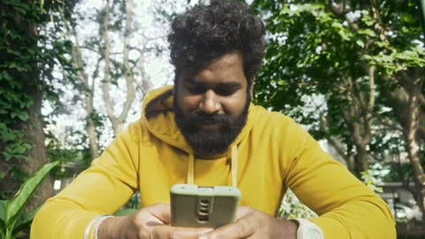 Man with a yellow outfit using a smartphone in a park,Indian male model with gre Stock Footage 166393505