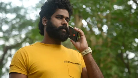Man with a yellow outfit using a smartphone in a park,Indian male model with gre Stock Footage 166447411