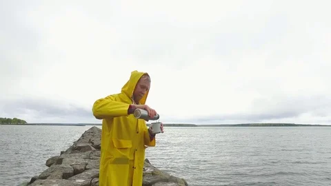 A man in a yellow raincoat drinking tea on a stone pier Stock-Footage 89880558
