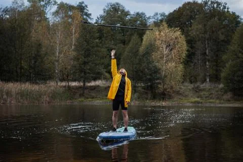 A man in a yellow raincoat throws an oar while standing on a paddleboard, Stock Photos