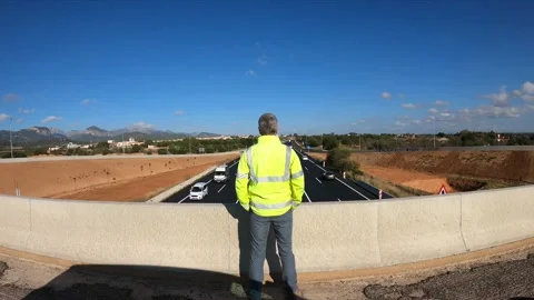 Man in a yellow safety jacket standing from a bridge looking at the traffic Stock Footage 151887872