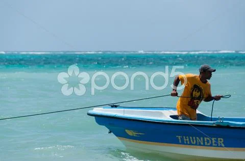 Man With Yellow Shirt And Hat On Fishing Boat Pulling A Rope In The Ocean