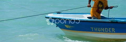 Man With Yellow Shirt And Hat On Fishing Boat Pulling A Rope In The Ocean