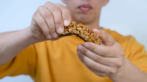 Man in a yellow sweater breaks protein bar close-up, selective focus. Stock Footage 163785257