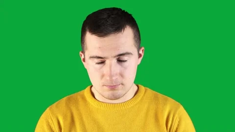 Man in a yellow sweatshirt winks looking at the camera on a green background Video stock 160989627