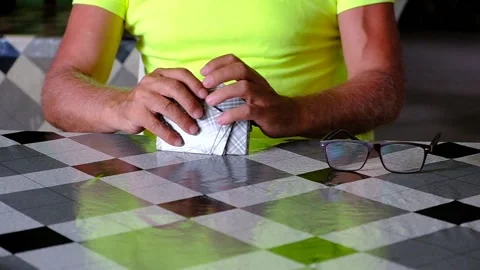 A man in a yellow T-shirt shuffles a deck of playing cards. Stock Footage 135377553