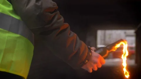 Man in yellow vest sets fire to a Molotov cocktail in a dark alley. Back view Stock Footage 99476696