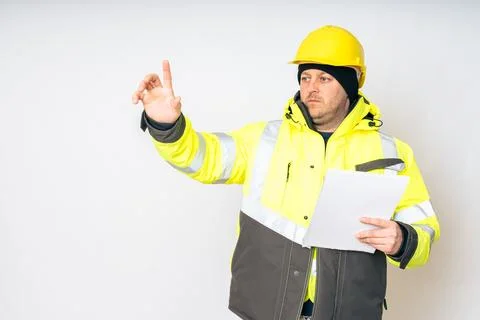A man in a yellow working winter jacket, yellow safety helmet with papers in his Foto stock