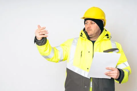 A man in a yellow working winter jacket, yellow safety helmet with papers in his Foto stock