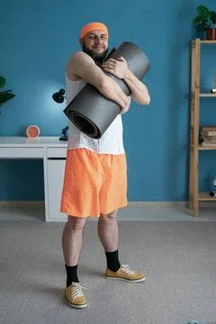 Man with yoga mat is ready for exercise in a bright living room, showcasing.. Stock Photos