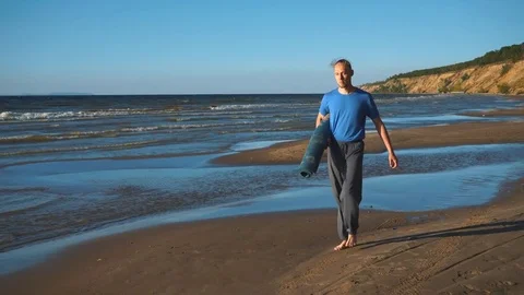A man with a yoga rolls walking on the beach Stock Footage 80794568