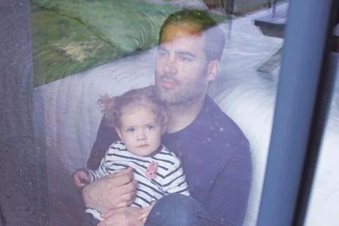 Man with young child looking through window watching rain fall Stock Photos