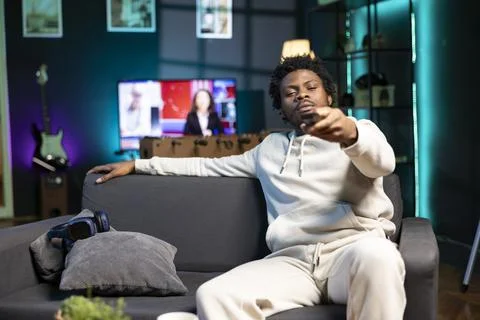 Man zapping through TV channels using remote, relaxing on couch Stock Photos