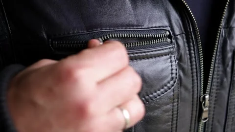 The man zips up the pocket of his leather jacket. Metal zipper in outerwear Stock Footage 323766077