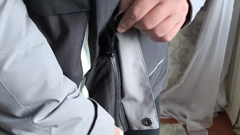 A man zips up a warm winter jacket in close-up. Down jacket for cold weather. Stock Footage 325034060