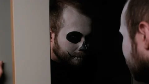 A man in zombie make-up in bathroom in front of the mirror and looks at himself. Video stock 142075662