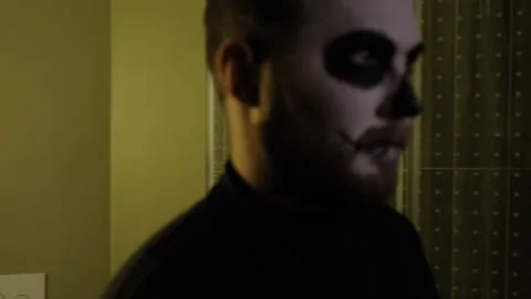 The man in zombie makeup walks, stops, looks around and leaves frame.Halloween Video stock 142076260