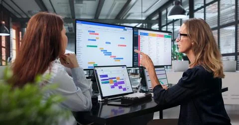 The Manager And Assistant Discuss Project Deadlines Using A Digital Schedule. Stock Photos