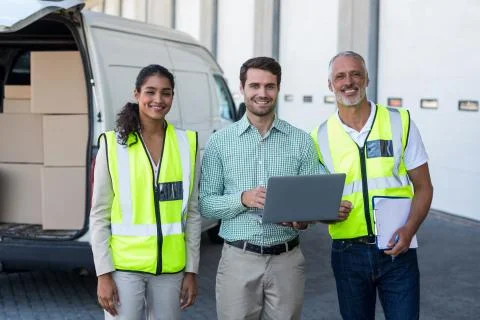 Manager and warehouse workers standing with laptop and clipboard 스톡 사진