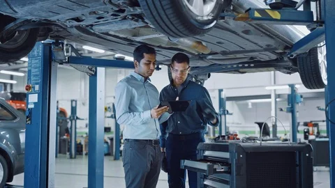 Manager Checks Data on a Tablet Computer and Explains the Breakdown to Mechanic Stock Footage 125797336
