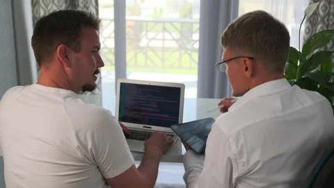 Manager discusses app ideas with a programmer, reviewing code on a laptop. Stock Footage 294298850