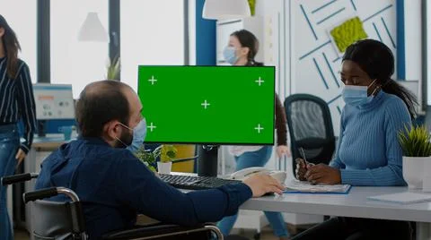 Manager with face mask typing on pc with green screen discussing with african 写真素材