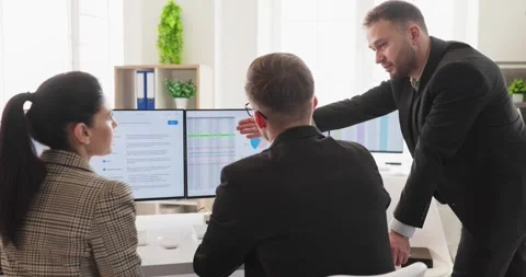 Manager guiding business team through data on dual monitors in modern office Stock Footage 344463446