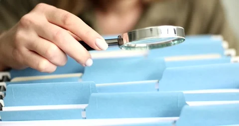 Manager looking for document among many folders with papers using magnifying Stock Footage 261845790