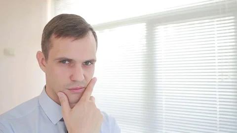 The manager looks thoughtfully at the camera on the background of the blinds in Stock Footage 74103013
