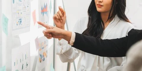 Manager with suit pointing at whiteboard to his female colleague Intellectual. Stock Photos