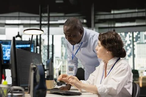 Manager supervising intern in office automating tasks using AI scripts on PC Stock Photos