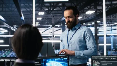 Manager supervising work of server room engineer using AI Stock Photos