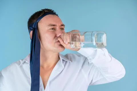 Manager with a tie on his head drinks alcohol from the bottle throat standing Stock Photos