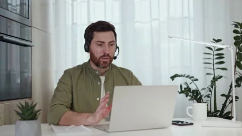 Manager typing on laptop and talking in headset during meeting at apartment Stock Footage 262222445