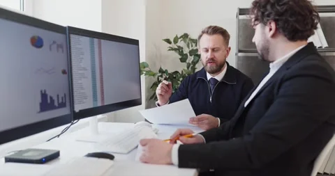 Managers discussing analytics with coworker at dual monitors in modern office Stock Footage 348200833