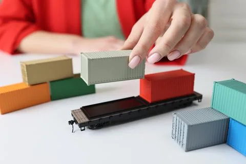 Manager's hand arranges cargo containers and railcars on table. Stock-Fotos
