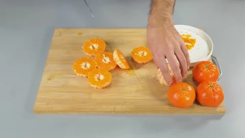 The mandarin fruit is being peeled over a cutting board. The chef is peeling by Video stock 233217627