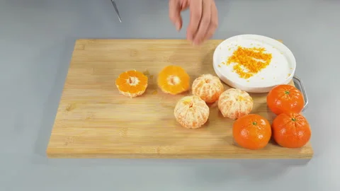 The mandarin fruit is being peeled over a cutting board. The chef is peeling by Stock Footage 233217792